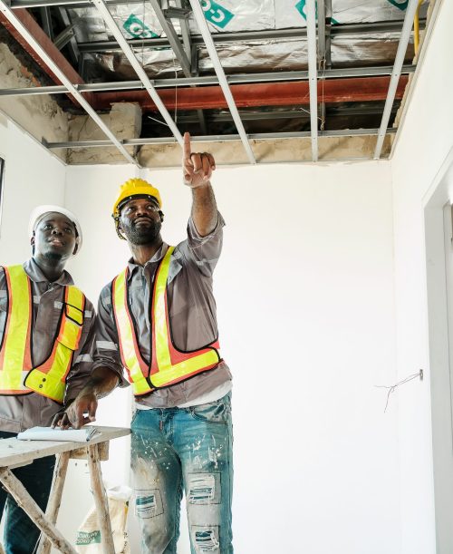 Two construction workers in safety gear inspect a ceiling during an interior renovation. Site supervision, teamwork, and building progress concept in real estate and property development.